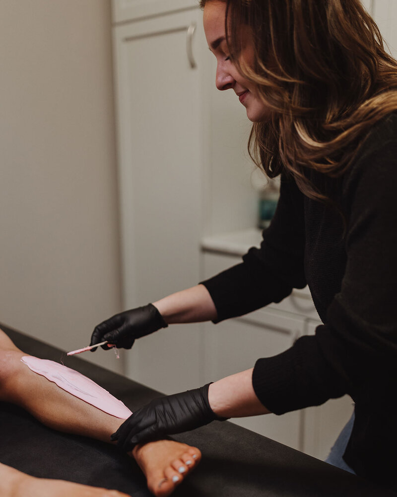 Esthetician applies pink hard wax to client's leg for waxing