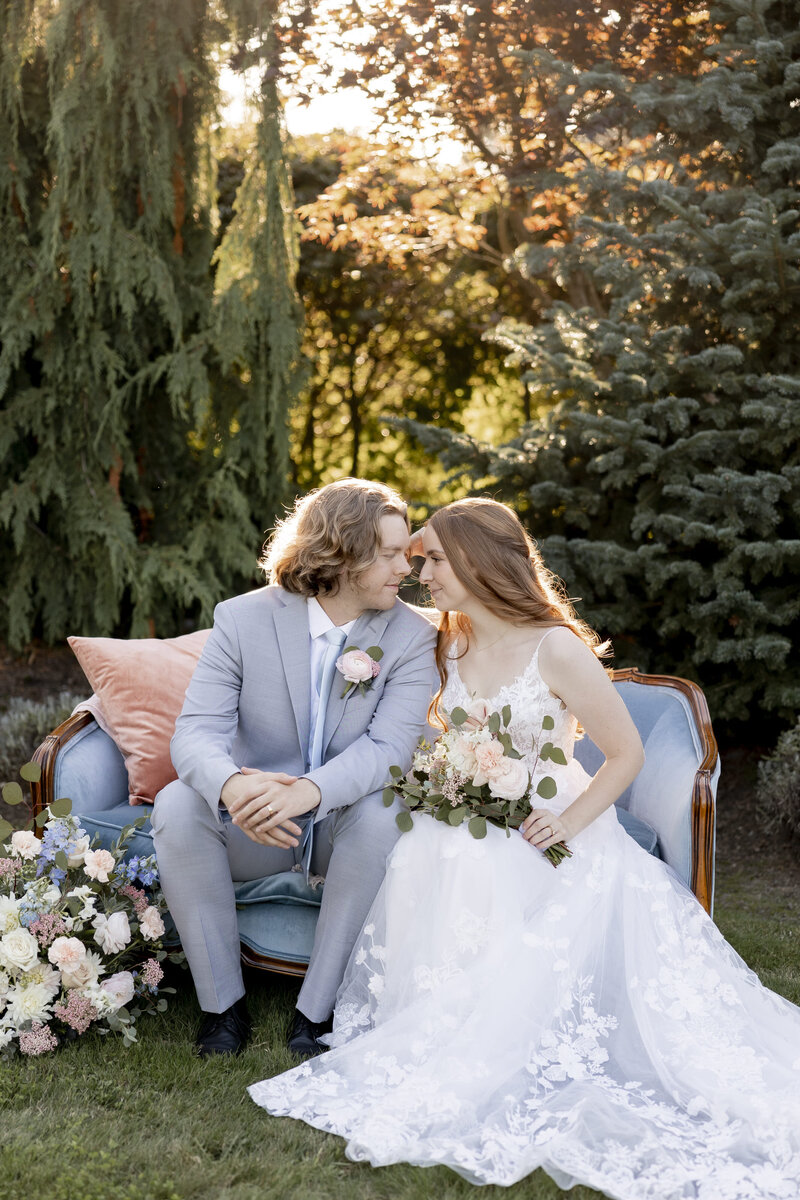 Bride and groom sitting on a blue couch surrounded by greenery