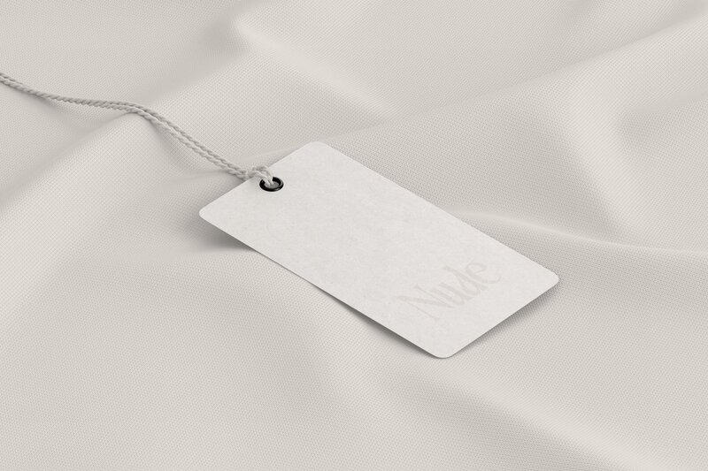 Clothing tag with the 'Nude' logo, attached to a soft, textured fabric, representing the swimwear brand's minimalist and sophisticated branding.