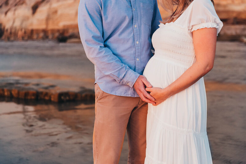 close up of a man and woman with their hands on the woman's baby bump