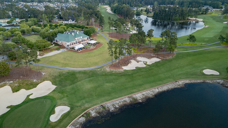 Aerial view of Woodcreek Country Club in Columbia, SC, showcasing the clubhouse, manicured golf course, and scenic water features. A gathering is visible on the terrace, with white tents set up for an event. Capturing professional branding photography for country clubs, golf courses, and luxury event venues in South Carolina.