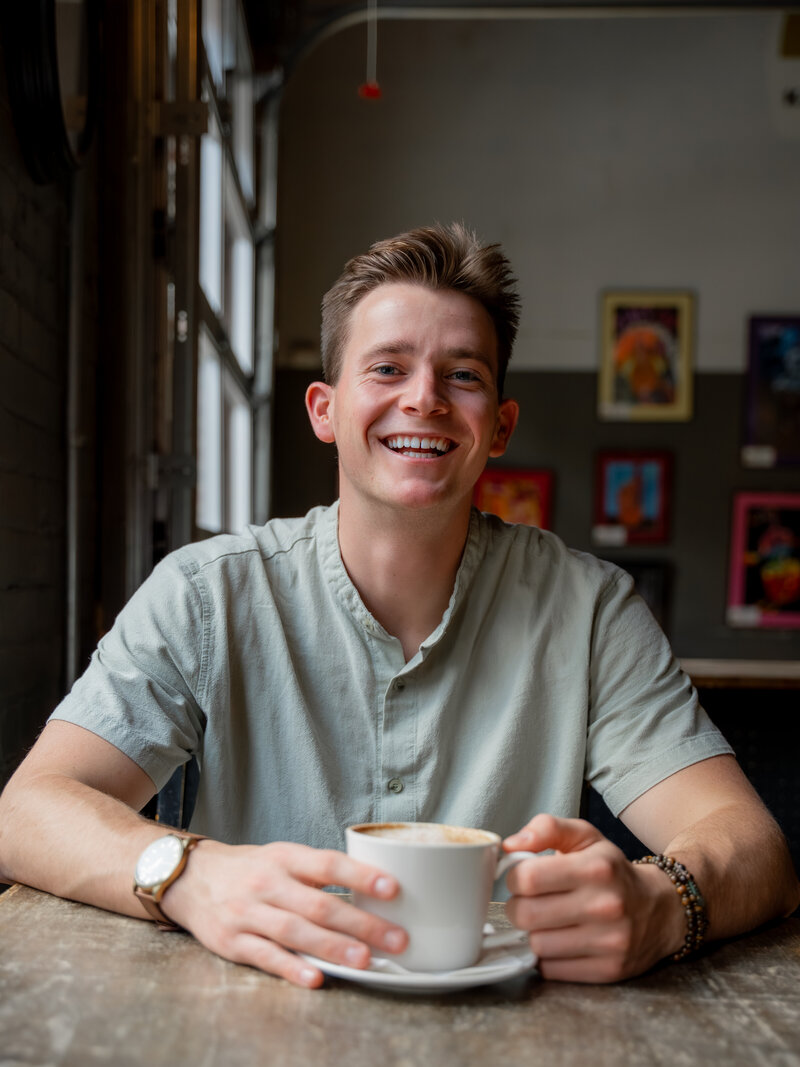 Isaac smiling while holding a cup of coffee
