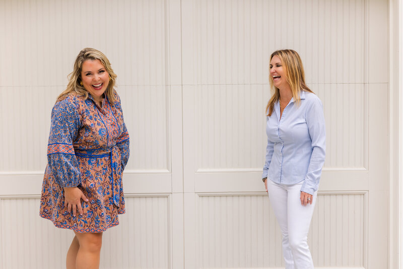 women wearing coordinated white, pink and blue outfits standing in front of a white wall and laughing during photoshoot
