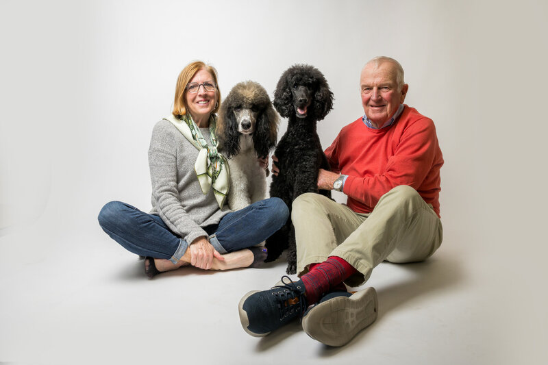 Couple with their two poodle pets sit together and smile for family portraits