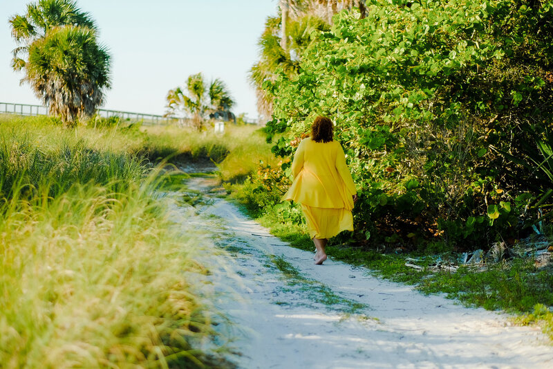 Certified life coach Claudine Martinell walking amidst greeneries in a radiant yellow dress.
