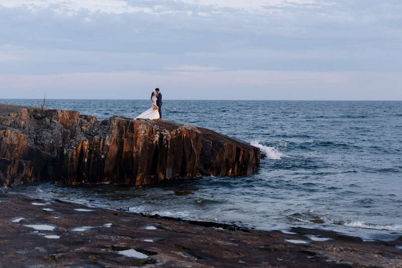 Couple shares a quiet moment during a sunset elopement on a cliff, captured by an adventurous wedding photographer.