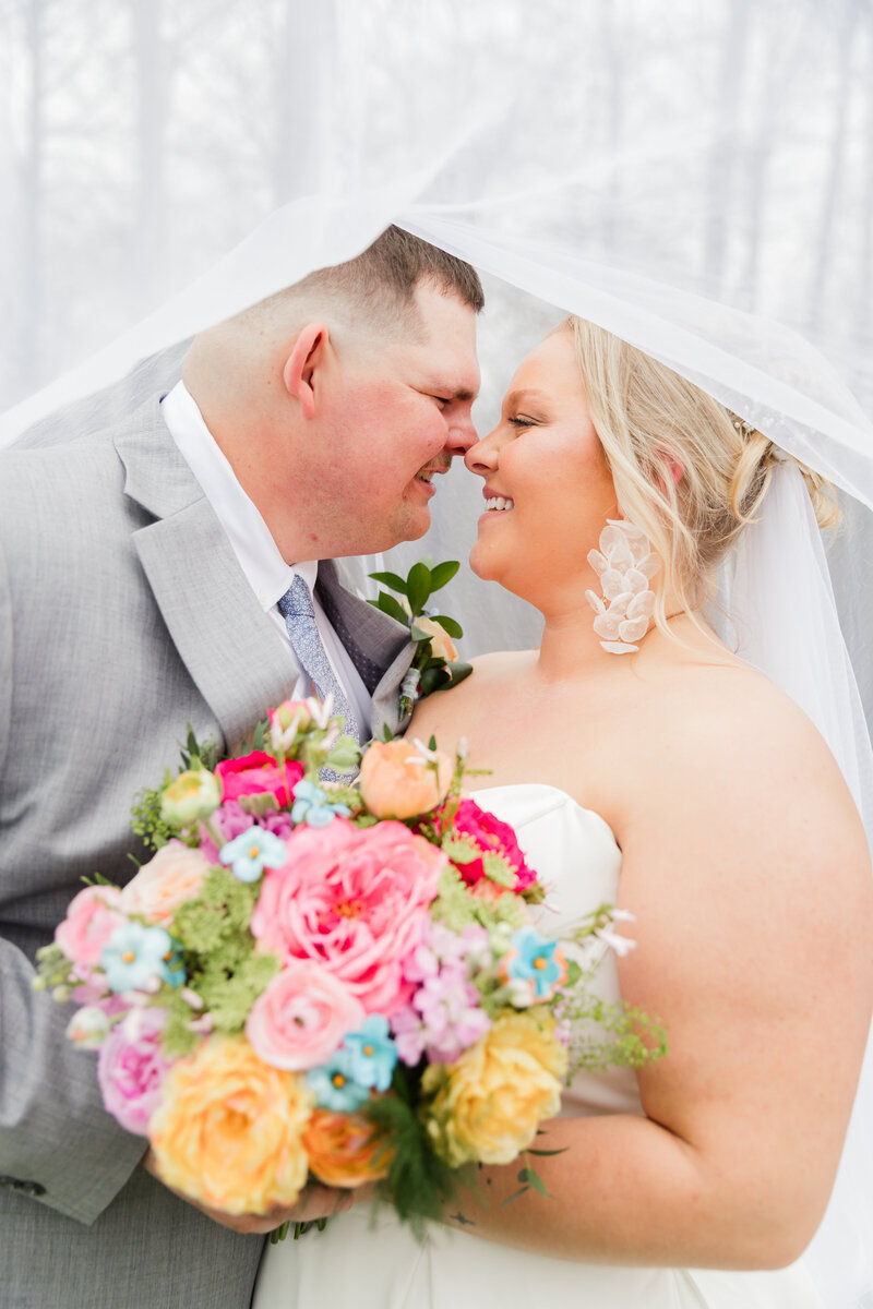Bride and groom exchanging vows in a lush greenhouse filled with vibrant greenery and blooming flowers, with sunlight streaming through the glass windows.