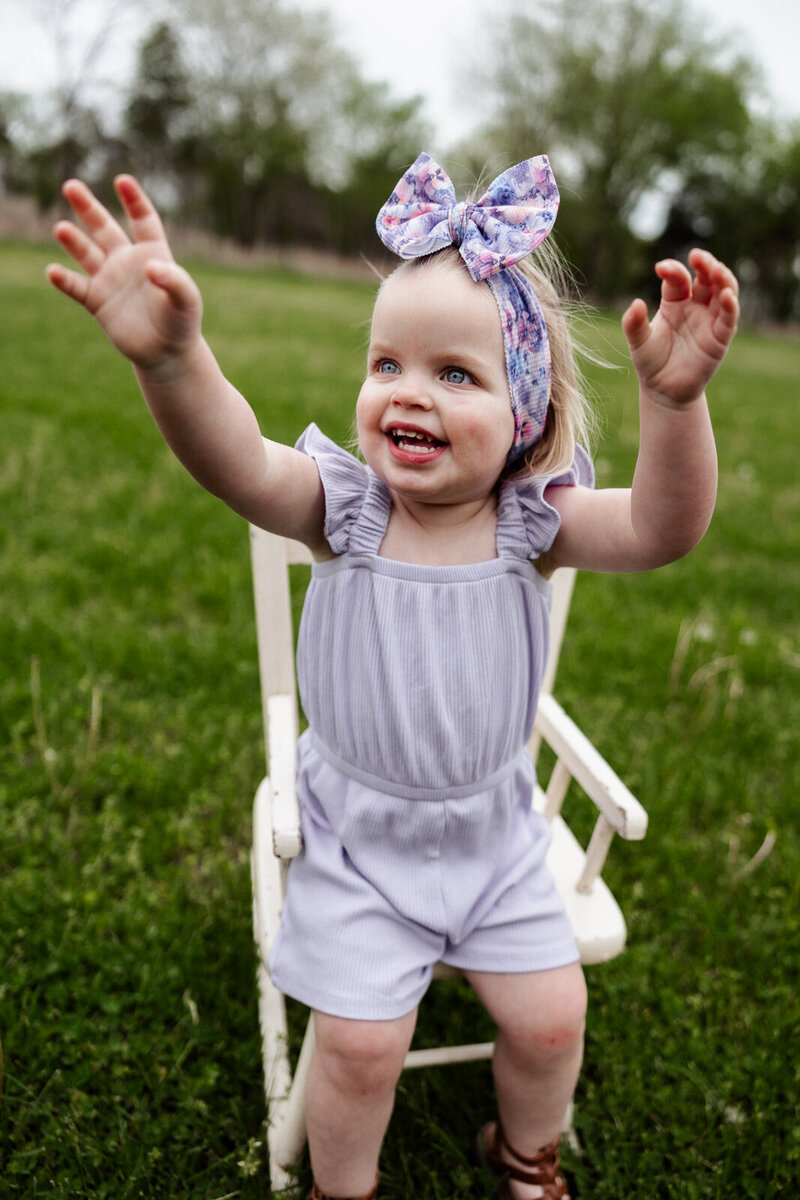 Portrait of a toddler girl smiling and jumping up from sitting in a chair excited.