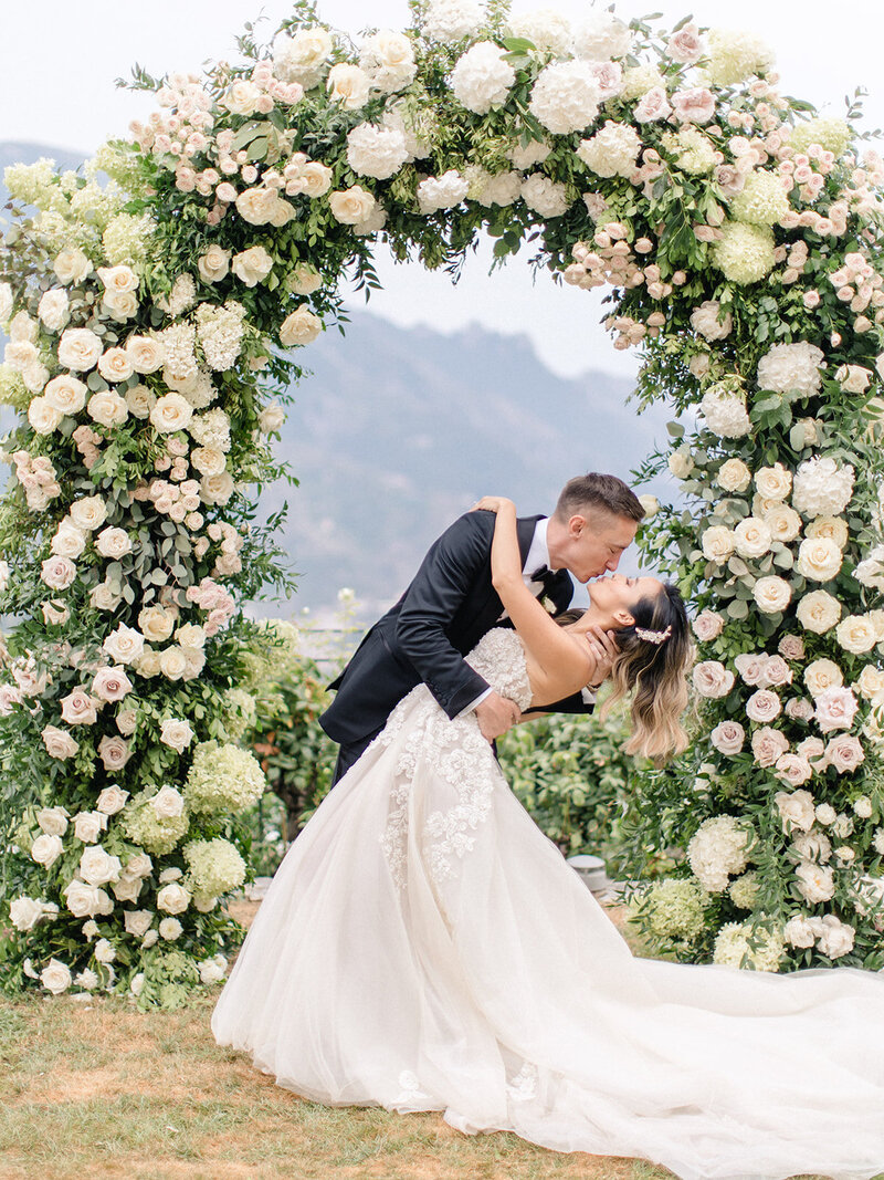 groom dips bride with luxury floral wedding arch