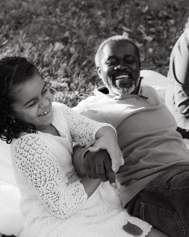 Black and white photo of a family of five standing together in a grassy field, capturing authentic, emotional moments and the quiet connection of everyday family life