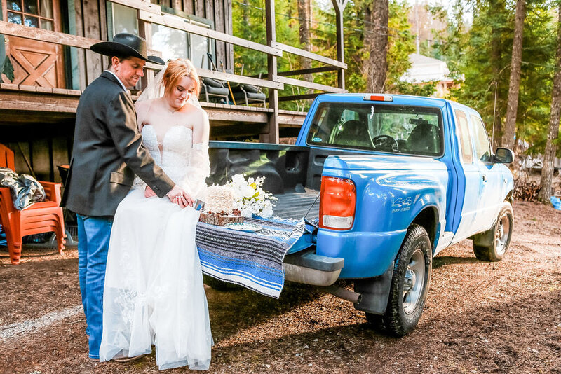 Bride and groom cutting wedding cake sitting in the back of a blue truck