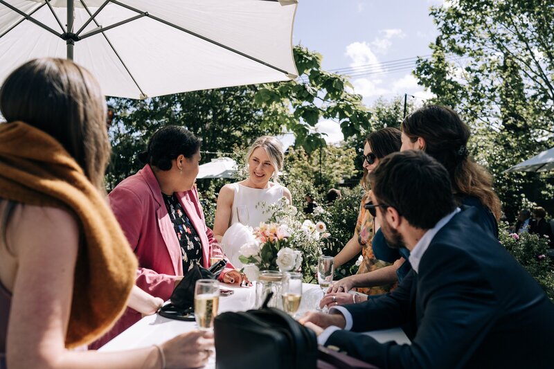 wedding guests have a drink under a white umbrella from little hire company