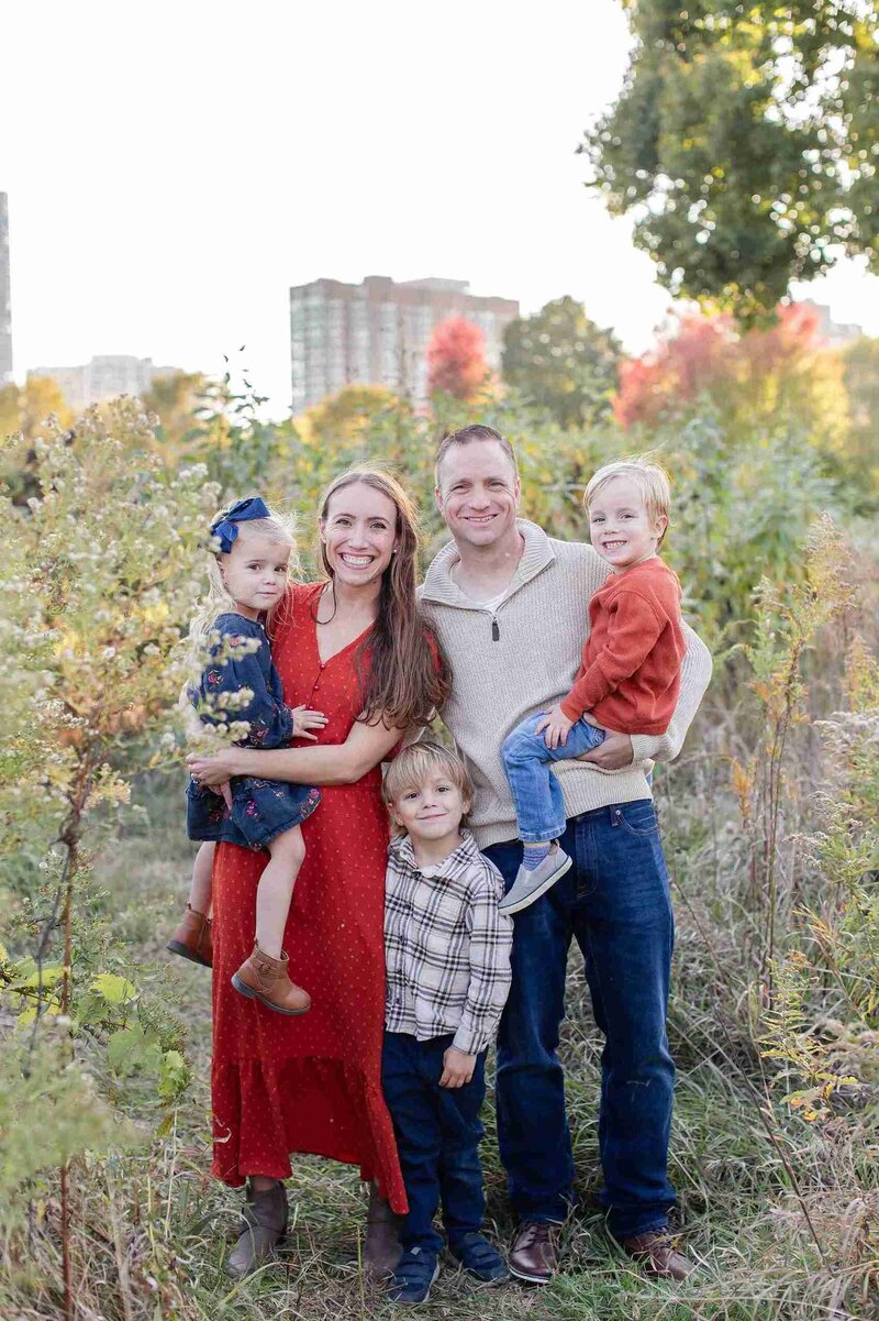 A family smiles together in a fall setting, captured by their Chicago photographer, with colorful leaves in the background.