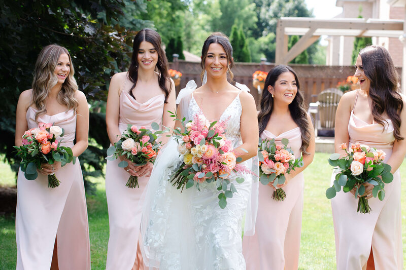 Ottawa wedding photos of a bride walking and laughing with her bridesmaids who are dressed in pink dresses