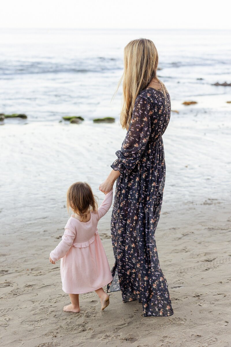 mom walks along Malibu beach while holding daughter's hand