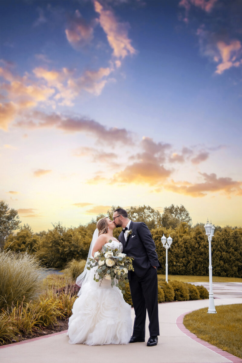 Bride and groom kiss under beautiful sunset sky
