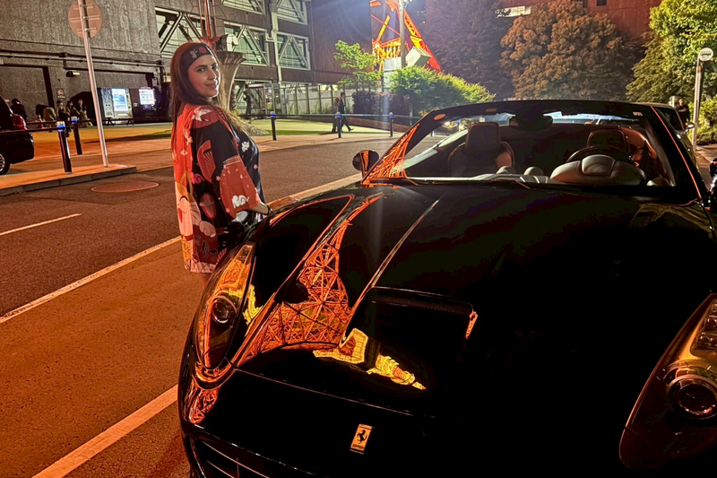 A woman in a traditional kimono stands next to a sleek black Ferrari under the glowing Tokyo Tower lights, with the tower’s reflection shimmering on the car’s hood.