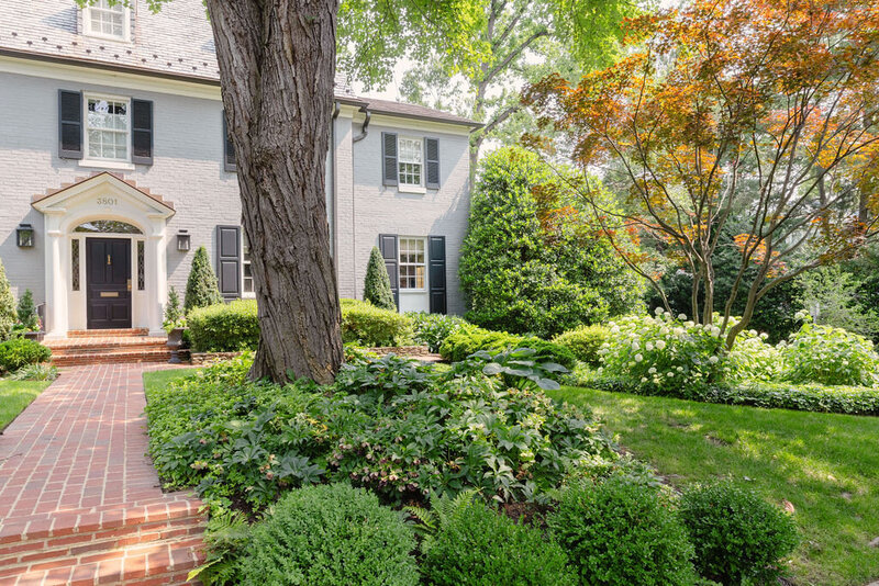Front yard of elegant home with brick pathway leading to front door surrounded by lush landscape