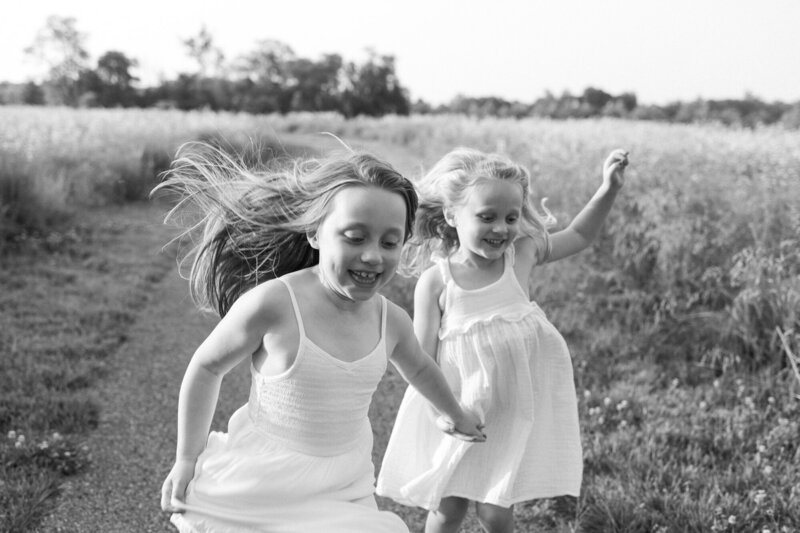 Black and white portrait of two little girls running through a field holding hands