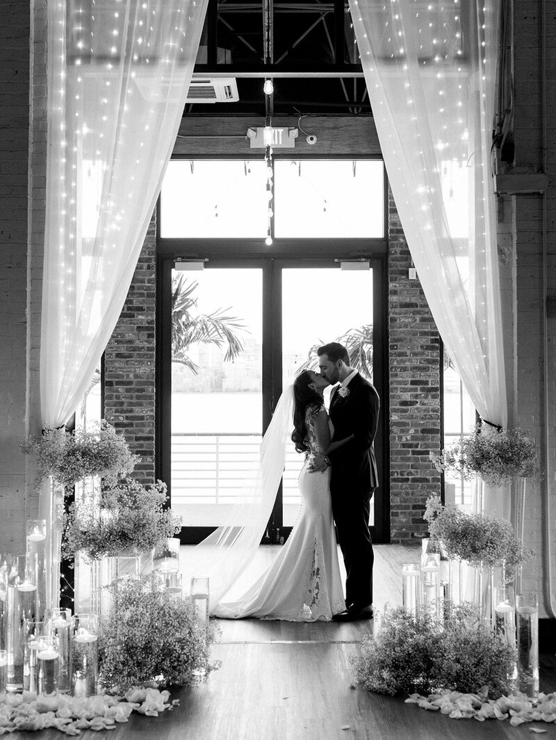 The bride and groom share a kiss in the doorway at their wedding while taking portraits together.