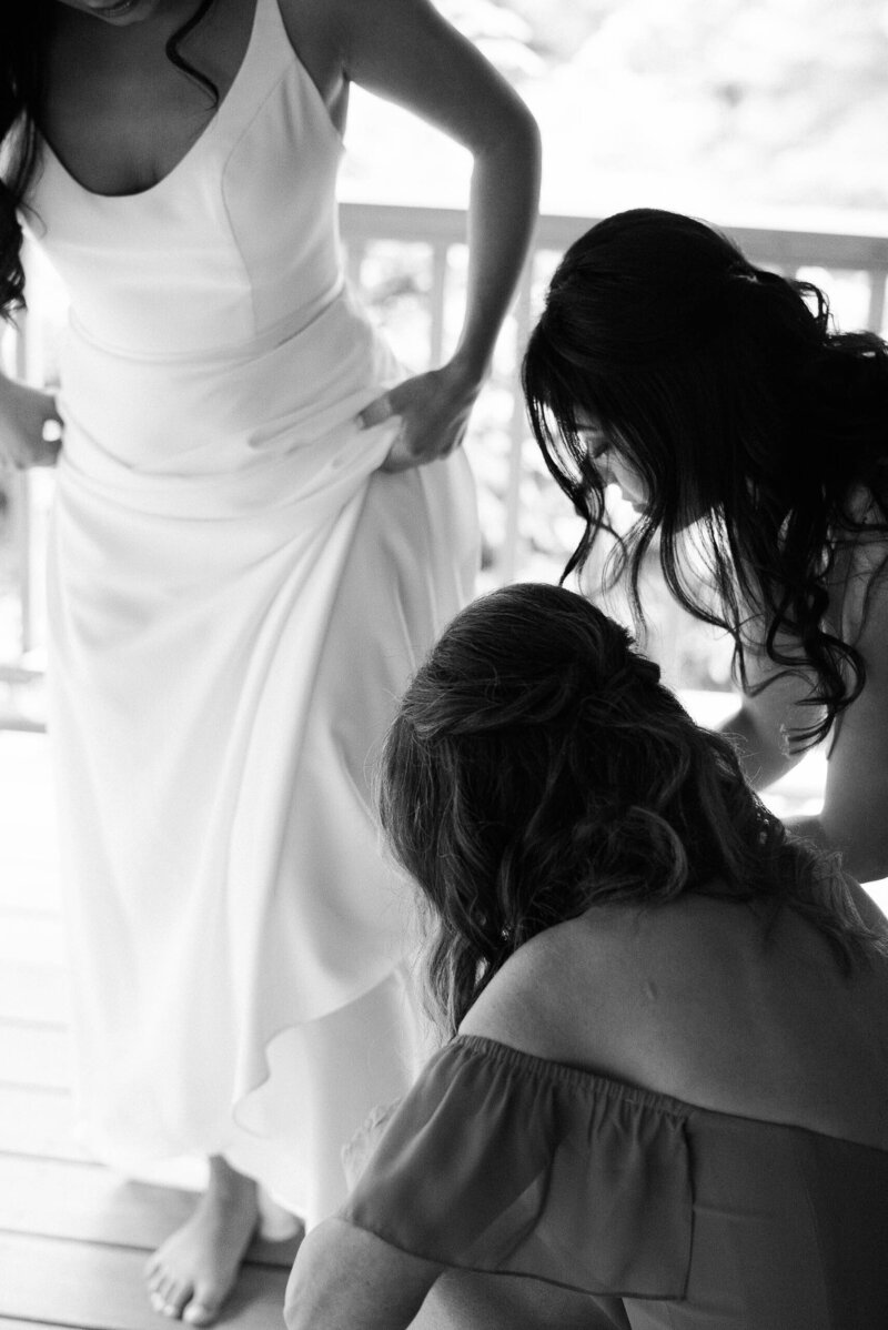 Bridesmaids kneel to help bride put on heels