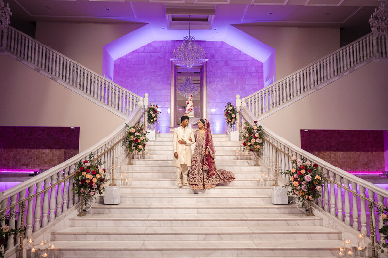 Gulanz & Faz holding arms as they pose on the grand stairwell at the famous bellevue center in chantilly virginia with led lighting