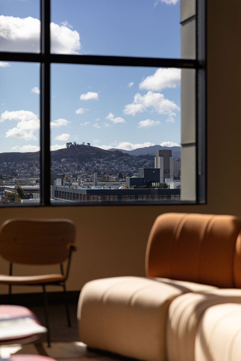 Cozy seating area with tan sofa and city skyline visible through large windows.