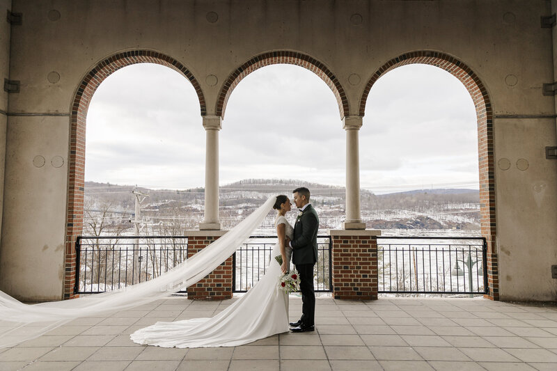 Bride and groom framed by stone arches overlooking the Hudson River on their wedding day