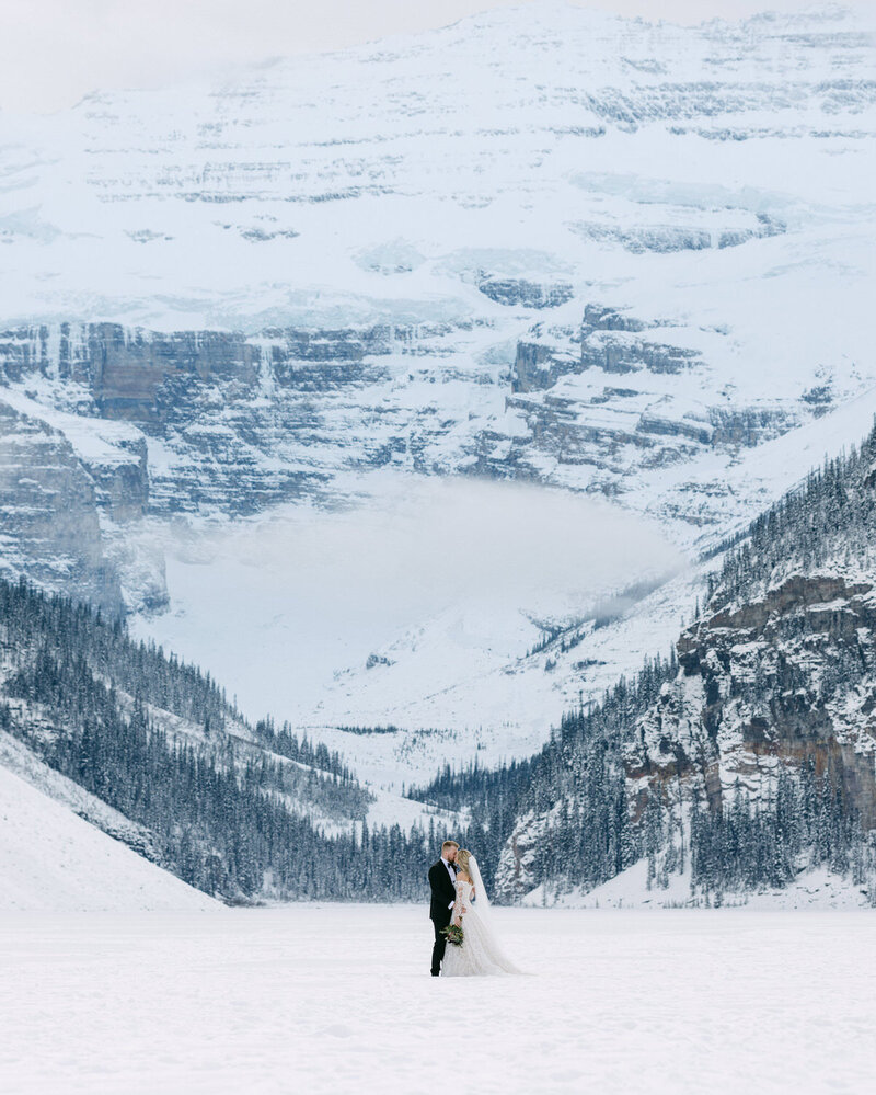 This breathtaking photograph captures the bride and groom kissing with joy after their luxury elopement in Banff National Park. Having just landed from their private helicopter, the stunning mountain landscape surrounds them, creating an unforgettable moment of celebration and love.