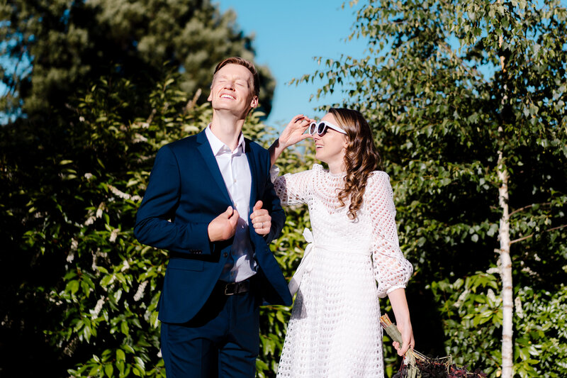 A fun wedding photo with the bride and groom looking up into the sun, the bride is dipping her white sunglasses
