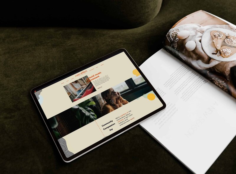 A tablet displaying a Showit web design rests on a couch next to an open magazine with a plate of cookies on top.