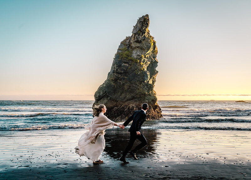 a couple in their wedding attire run on a rocky beach during their sunset elopement package