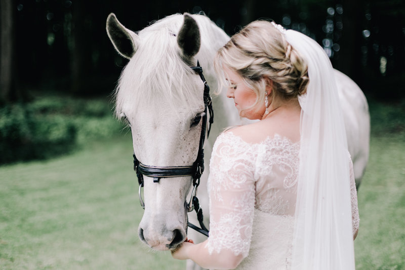 bruid in witte trouwjurk met sluier aait haar witte paard