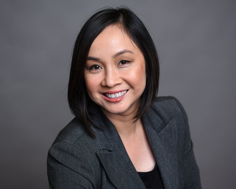 Professional headshot of a Toronto-based female executive with an open smile, wearing a grey suit against a light gray background