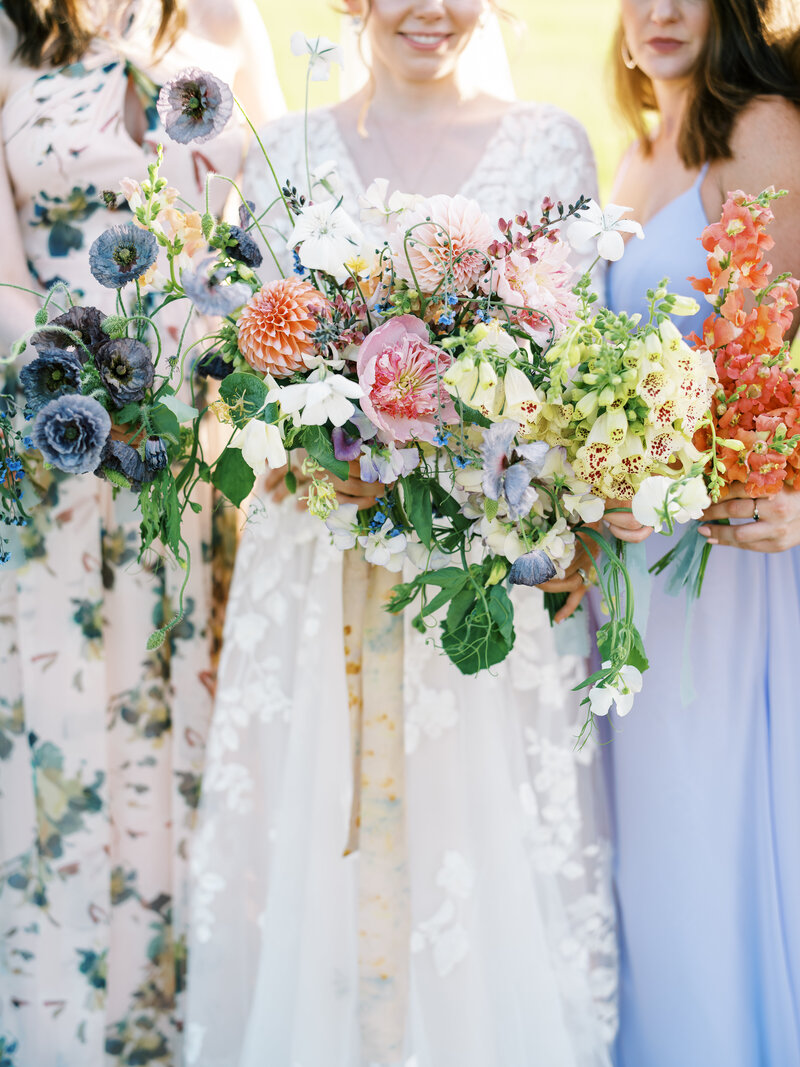 A colorful bride's rainbow bouquet of flowers with her bridesmaids photographed by Colorado Wedding Photographer JKG Photography