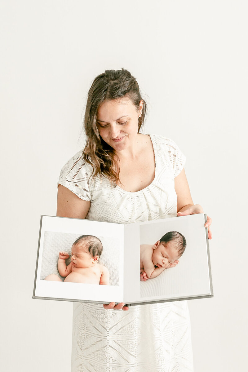Woman holding newborn photo album looking down | portland newborn photographer