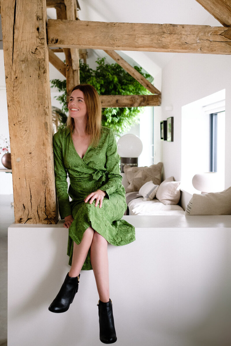A woman strikes a pose in front of a large window, with gentle natural light creating soft shadows around her.