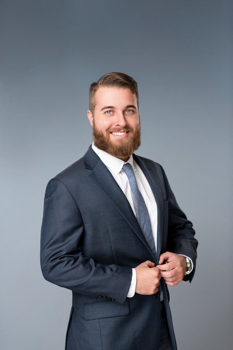 Man buttons his jacket in his blue tone headshot that is photographed like a GQ magazine