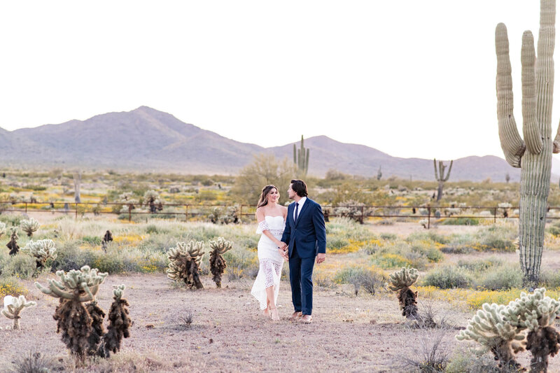 Bride and groom walking towards the camera looking at each other with mountains and lots of cacti in the background