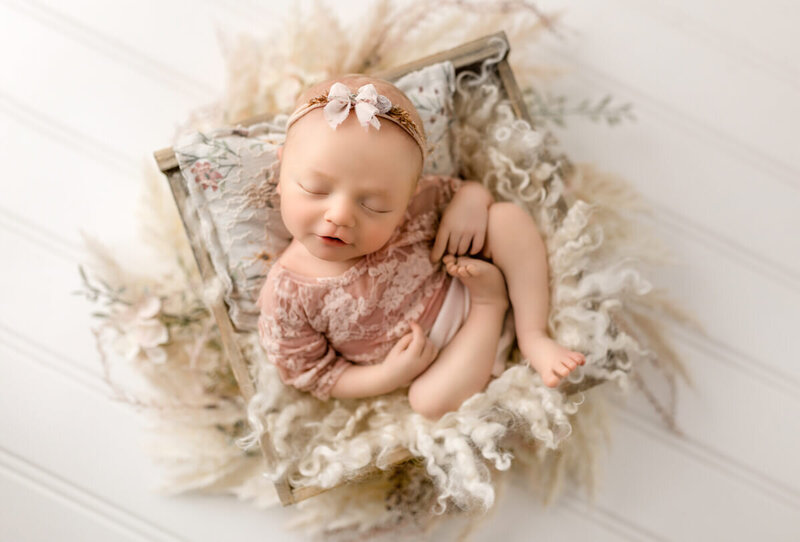 Newborn baby wearing a simple floral headband, asleep on a textured blanket, photographed in an elegant fine-art style.