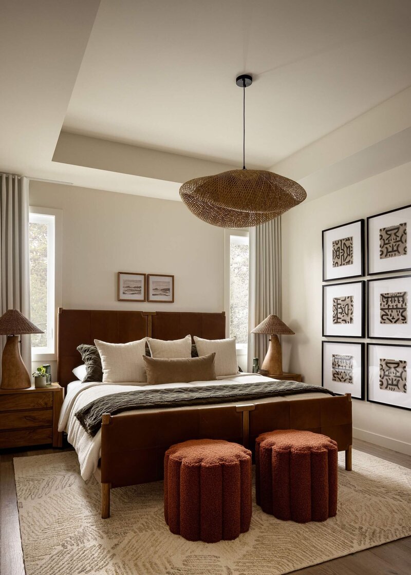 Soothing Japandi-inspired primary bedroom with a genuine leather bed, rattan light fixture, textured boucle ottomans, earthy abstract art, and cozy layered textiles.