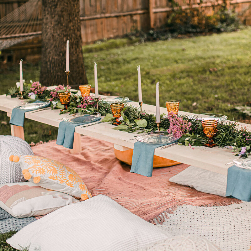 Table colorée, style bohème, dressée dans un jardin avec coussins autour pour l'organisation d'un EVJF