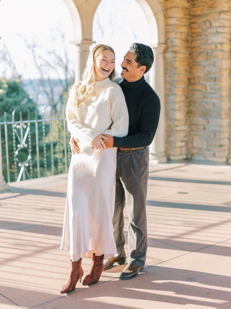 Couple laughing under arches during winter Alms Park engagement photos in Cincinnati photographed by Catholic wedding photographers Laura and Matthew