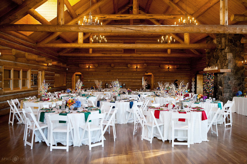 White tables and chairs decorated with rainbow decor for a summer wedding inside Evergreen Lake House