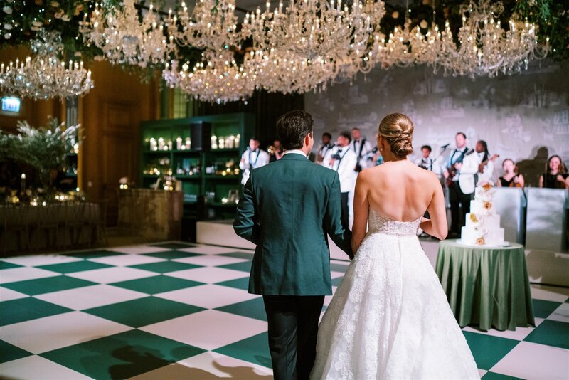 Bride and groom walking into a ballroom with crystal chandeliers and a large band and a green and white checkered dance floor