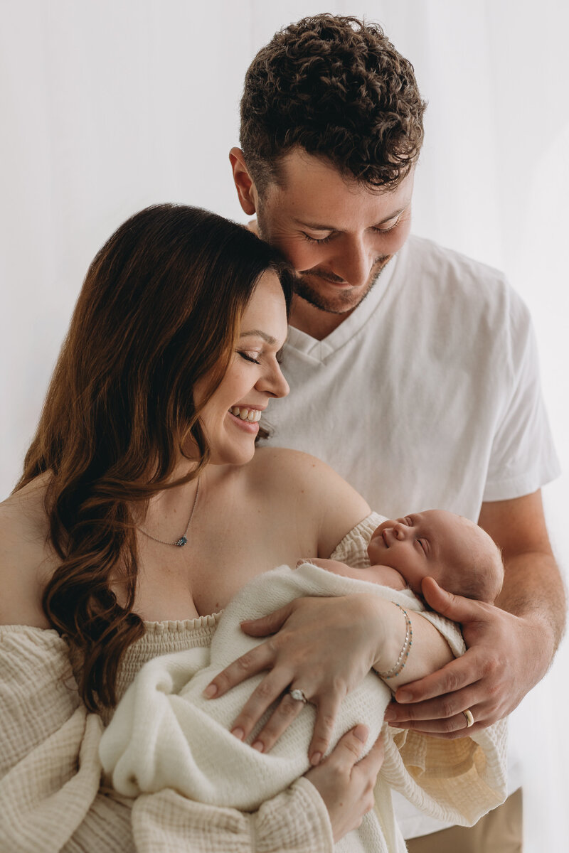 Newborn photos in kelowna b.c. with baby's parents giving baby a kiss and baby yawning