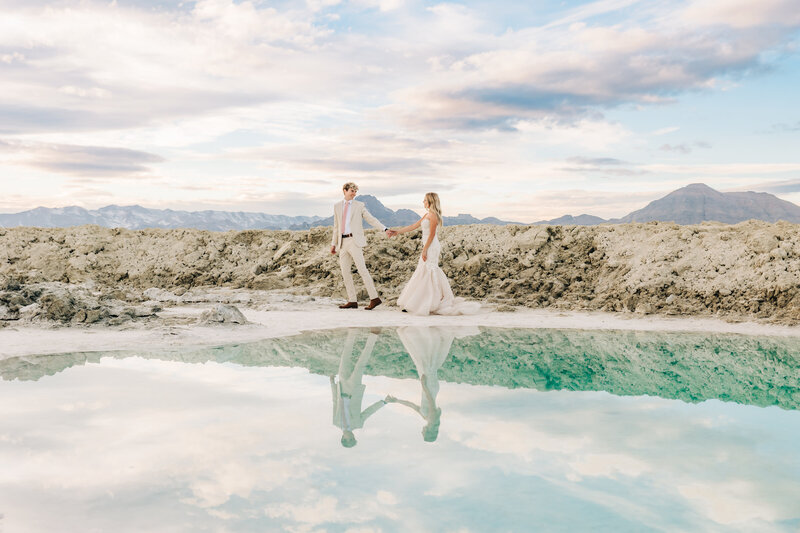 Newlywed couple holding hands along lake side