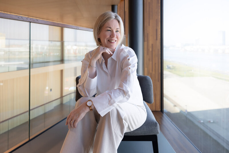 Vrouwelijke professional zit bij raam en zorgt voor verzuimpreventie in gezonde werkomgeving