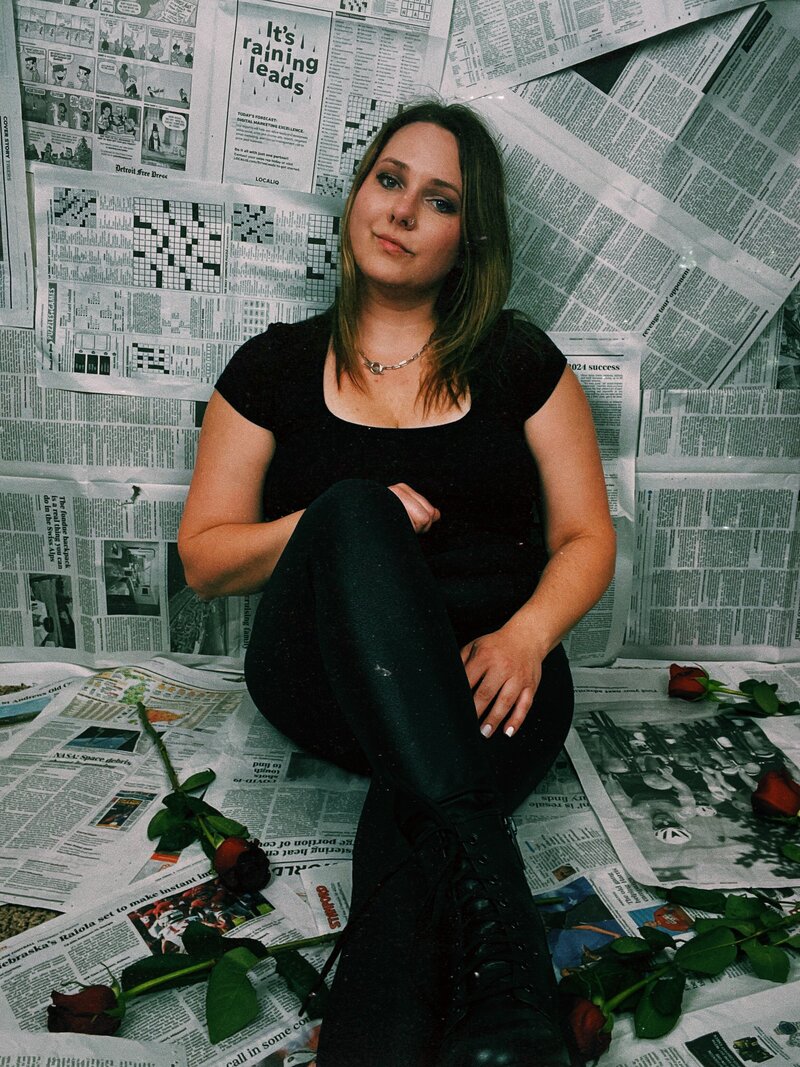 Kristina, a life coach for women, sitting on the ground with her legs crossed surrounded by roses smirking at the camera