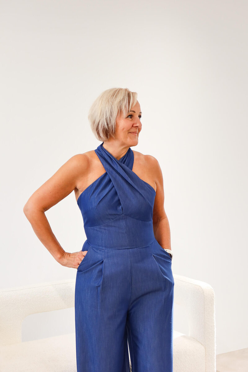 Woman standing confidently in a blue jumpsuit against a neutral background
